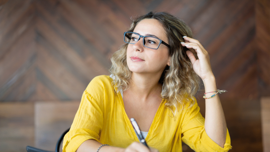 A woman with glasses staring off thinking about what to write.